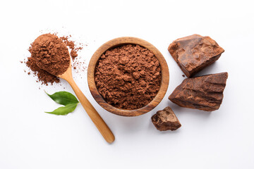 Cocoa powder in bowl, spoon, chunks and green leaves on white background, flat lay © New Africa