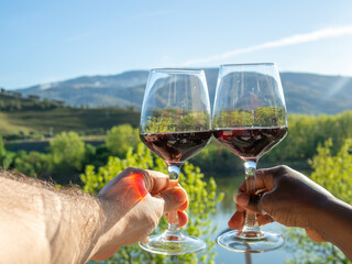 Naklejka premium Close Up of Hands Clinking Wine Glasses in Peso da Régua with Sunlit Douro Valley Mountains Behind