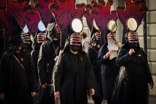 Basel, Switzerland - 10 March 2025: View of hooded figures with masks and mirrors marching in the Fasnacht parade, a sea of black against the muted city backdrop.
