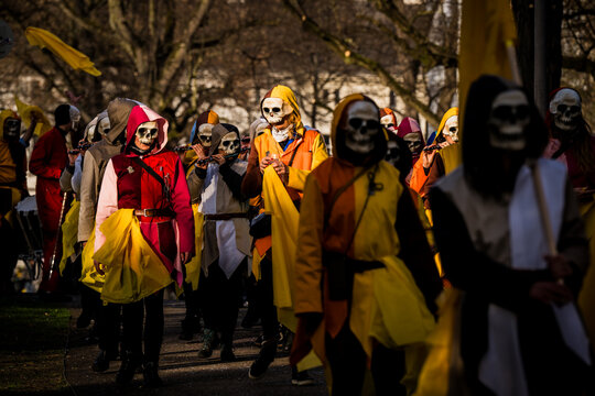 Basel, Switzerland - 10 March 2025: View of a parade of masked figures in vibrant costumes, a river of color and movement against the muted backdrop of trees.