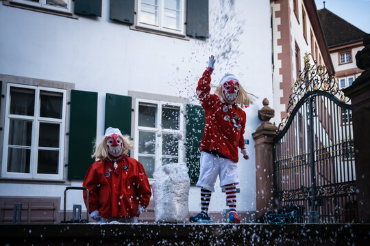Basel, Switzerland - 10 March 2025: View of two masked figures in red and white costumes playfully throwing confetti against a backdrop of classic architecture..