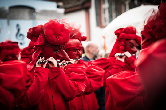 Basel, Switzerland - 10 March 2025: View of vibrant red-clad figures, masked and playing flutes during Fasnacht, a burst of color against the muted urban backdrop.