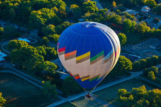 Albuquerque, United States - 11 October 2017: View of a vibrant hot air balloon drifts serenely above a patchwork of green trees and buildings, contrasting against the blue sky.