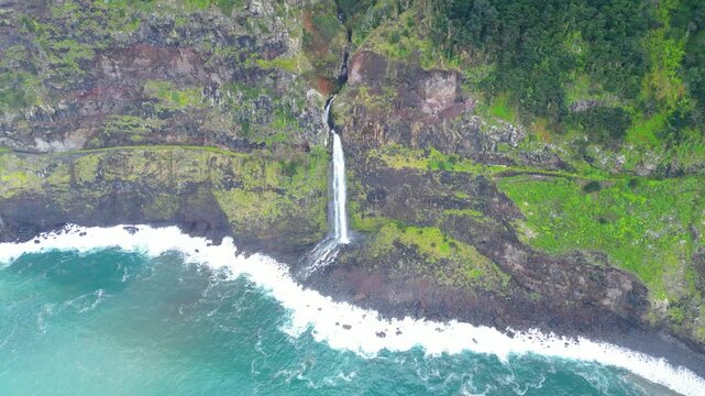 Aerial view of a stunning waterfall cascading down lush green cliffs into the vibrant turquoise Atlantic Ocean on Madeira's dramatic north coast. Nature's beauty. Miradouro do Veu da Noiva