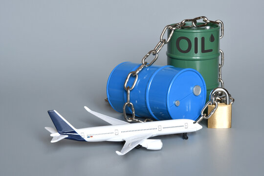 Miniature oil barrels locked with a chain and padlock, along with an airplane. Concept of the shortage and rising price of jet fuel due to the Middle East crisis and the war in Iran.