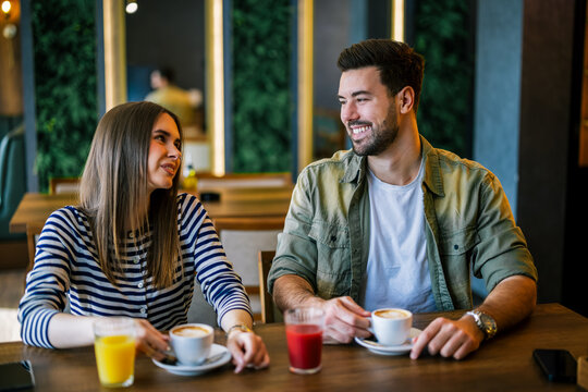 Candid moment of happy friends giggling and drinking coffee at a cafe.