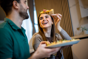Happy young couple sharing a pizza in their apartment as a woman feeds her partner.