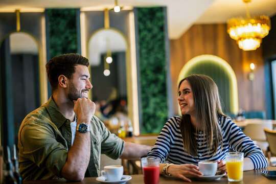 Two young friends laughing and talking in a cafe with coffee and juice.