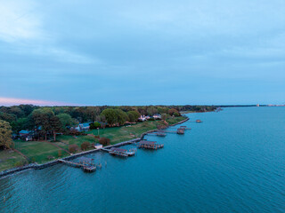 Fototapeta premium Aerial view of Newport News coastline along the James River, featuring a row of private wooden piers and boat houses along the grassy shoreline at dusk.