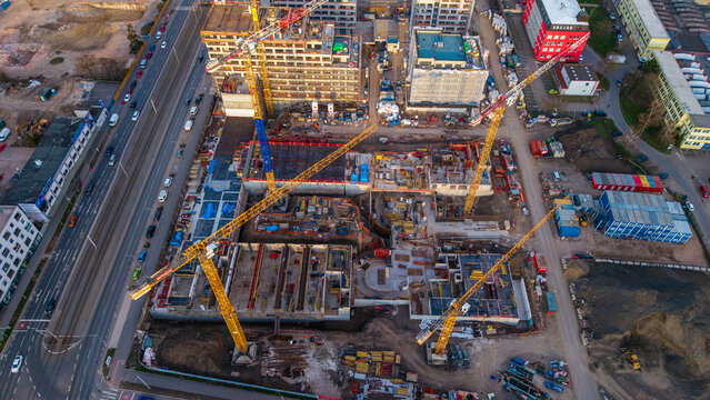 Aerial view of a construction site bustling with yellow cranes against the stark concrete foundations, contrasting with the surrounding buildings, Prague 9, Prague, Czechia.