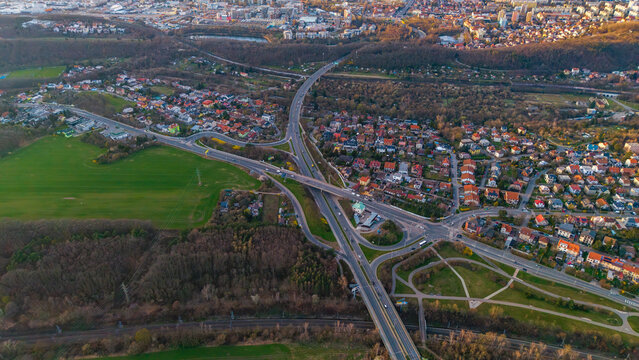 Aerial view of a sprawling highway intersection cutting through green fields and dense residential areas, a symphony of concrete and nature., Praha 9, Hlavni mesto Praha, Czechia.