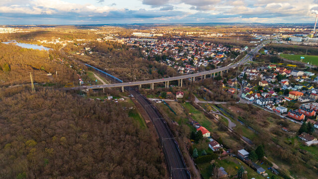 Aerial view of a modern bridge soaring over lush green forests and a railway line, with scattered houses adding a touch of human presence, Praha 9, Hlavni mesto Praha, Czechia.