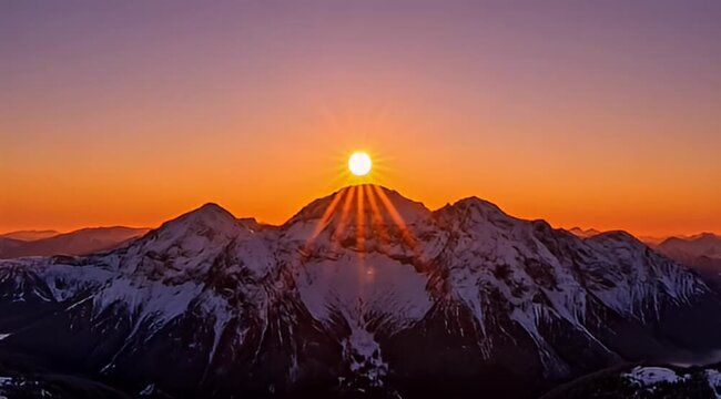 Magnificent sunset over snow capped mountains with radiating sun beams in alpine