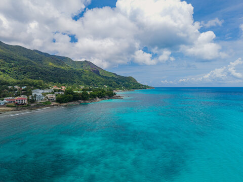 Aerial view of the turquoise waters meeting the lush green coastline dotted with buildings, a serene blend of nature and development, Victoria, Seychelles.