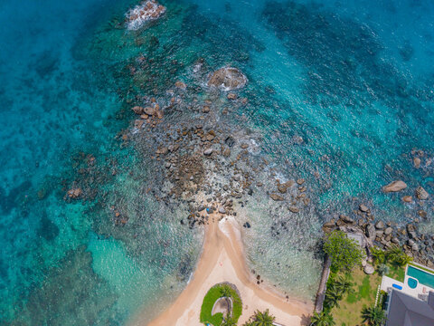 Aerial view of the turquoise ocean embracing the rocky shore, with a glimpse of sandy beach and lush greenery, Vista do Mar, Mahe Island, Seychelles.