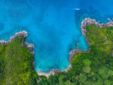 Aerial view of the turquoise sea meeting the verdant coastline with rocky outcrops and dense tropical foliage, Montagne Jasmin, Mahe Island, Seychelles.