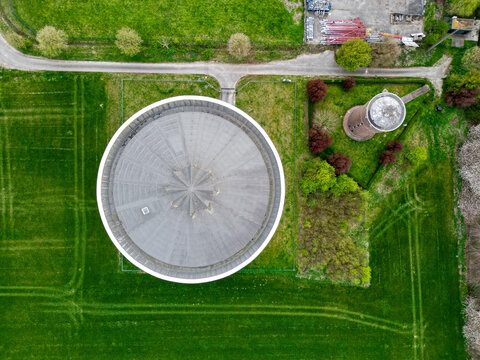 Aerial view of a water tower casting a stark shadow on the verdant field, a symphony of rural serenity, Ath, Wallonia, Belgium.