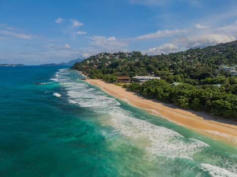 Aerial view of the shoreline where turquoise waters meet the sandy beach, framed by lush green hills, La Retraite, Mahe Island, Seychelles.