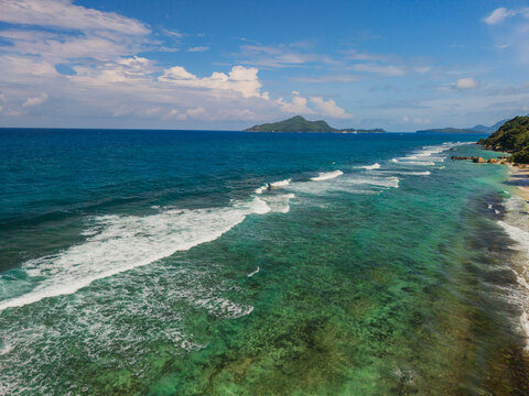 Aerial view of the vibrant turquoise waters meeting the sandy shorelines, with distant islands fading into the horizon, La Retraite, Mahe Island, Seychelles.