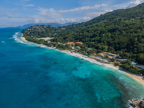 Aerial view of turquoise waters meet a pristine beach, fringed by lush green hills in a tropical paradise, La Retraite, Mahe Island, Seychelles.
