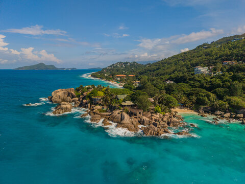 Aerial view of turquoise waters swirl around rocky outcrops, fringed by lush green hillsides and pristine beaches, La Retraite, Mahe Island, Seychelles.
