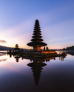 View of a multi-tiered pagoda reflecting in the calm, still waters under the soft glow of the dawn light, Bali, Bali, Indonesia.