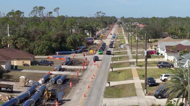 Street construction in Florida suburb with cars navigating single-lane traffic past construction vehicles, trenching machines and utility signs.