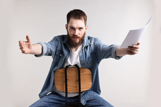 Professional actor with script performing on chair against light grey background