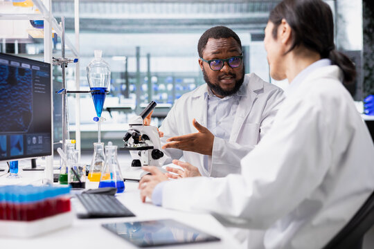 Lab scientists talking in workspace about genetic markers associated with disease risk. Asian man and coworker study DNA strand mapping with genomics analysis program on computer