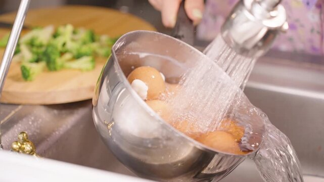 Slow Motion of Hand Washing Brown Eggs in Metal Bowl Under Running Water Near Chopped Broccoli on Board