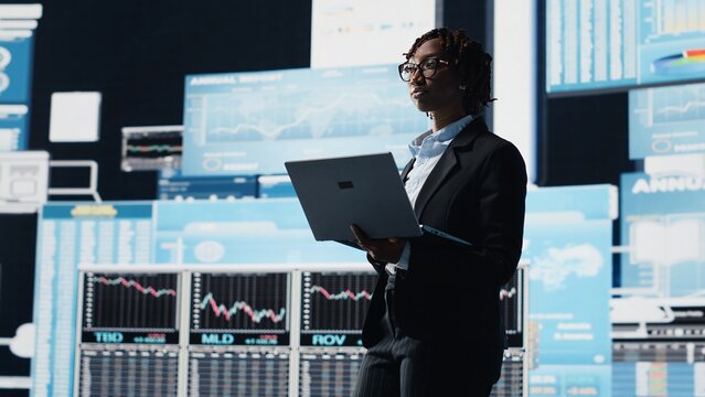 Business specialist using laptop to compare company KPIs data on digital videowall before making decisions. Leader analyzing enterprise corporation key performance indicators using notebook, camera B