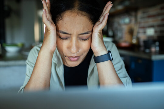 Stressed woman holding head while working at home kitchen
