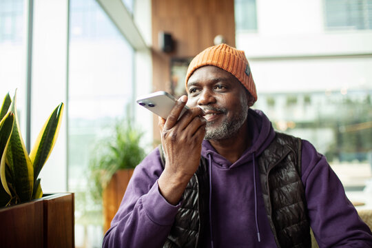 Smiling mature man using voice assistant on smartphone in cafe