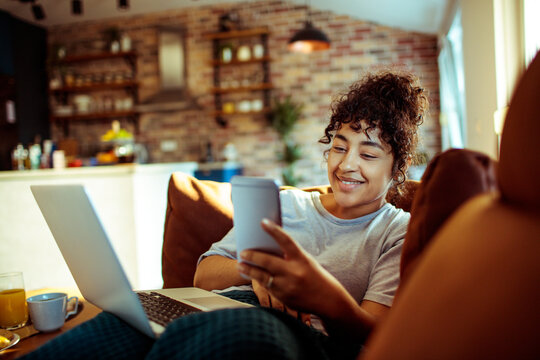 Young woman using smartphone and laptop at home