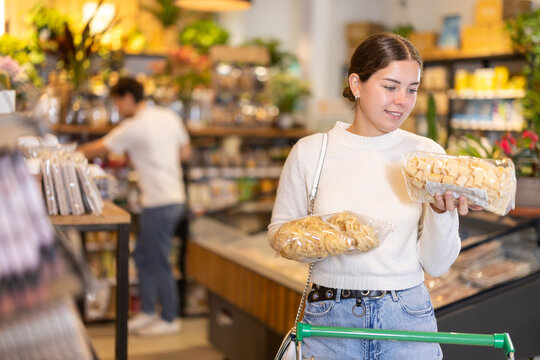 Girl compare and choosing pasta, doubt and think before buying. Client choose side dish food. Shop visitor pick up food in minimarket