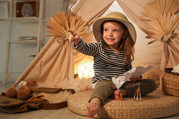 Little girl with drawing of map pointing at something near wigwam indoors © New Africa