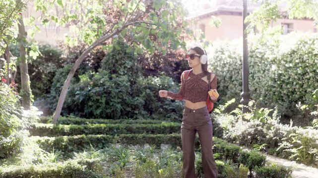 Joyful young woman dancing and listening to music in a sunny park