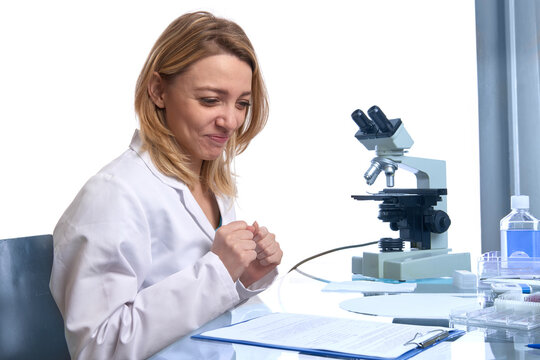 Young european female scientist with compound microscope reviewing lab notes at workstation