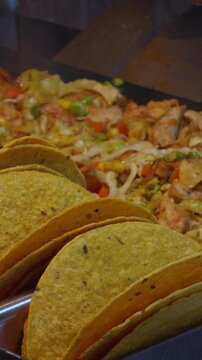 Vertical video. Fresh Hard-Shell Tacos Filled with Chicken, Cabbage, and Vegetables on Grill Station, Concept of Mexican Street Food Preparation