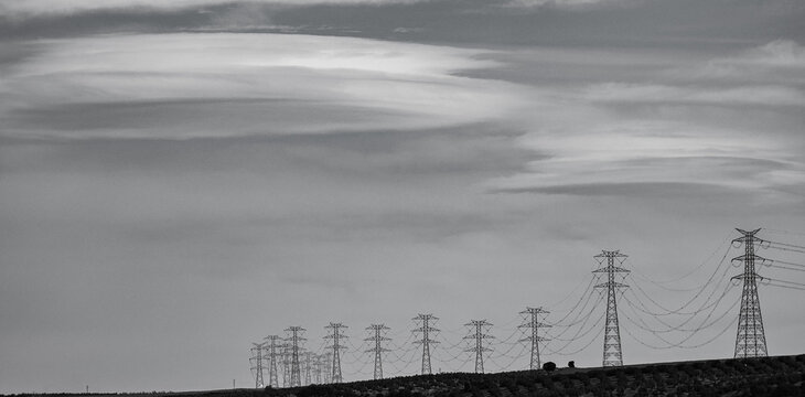 Black and white view of Electricity Pylons on a Hill Under a Cloudy Sky