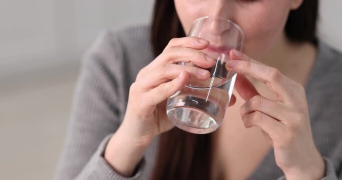 Woman with glass of water taking pill indoors, closeup