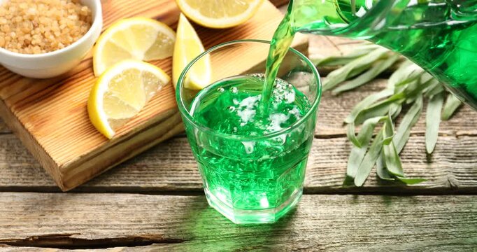 Pouring tasty tarragon lemonade into glass from jug on wooden table, closeup