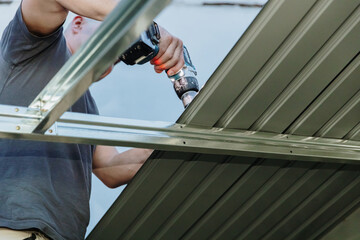 A mature roofer installs roofing sheets on a profile shed using a drill. © Nataliya