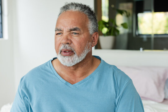 Senior African American male sitting on bed, gazing left, drawn by soft window light and mirror