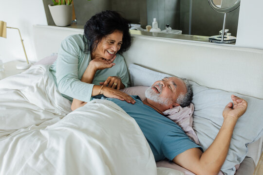 Senior African American couple woman leaning over man on bed, smiling and showing morning affection