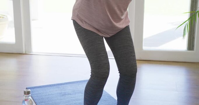 African American woman knees-bent, wearing pink top, rowing weights on mat by glass doors, toning