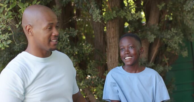 Man and boy high-fiving then sitting on ledge with solar panel, man teaching under trees
