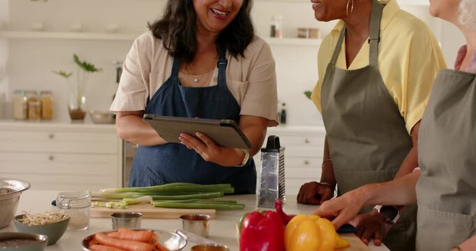 Diverse female friends following tablet steps at kitchen island, slicing peppers, preparing meal