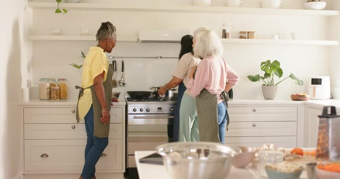 Meal prep starting, three women in aprons stirring and tasting at stove with metal bowl