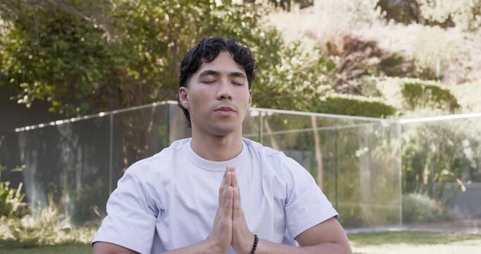 Asian man in mid 20s starting meditation, raising arms, joining palms, breathing by glass railing